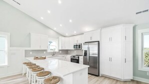 Uma cozinha moderna com armários brancos, uma geladeira de aço inoxidável e uma ilha central com banquetas.