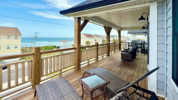 Um deck coberto com móveis de vime, corrimão e vista para o oceano.
