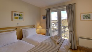 Ein Hotelzimmer mit zwei Betten, einem Balkon mit Blick und gerahmten Bildern an den Wänden.