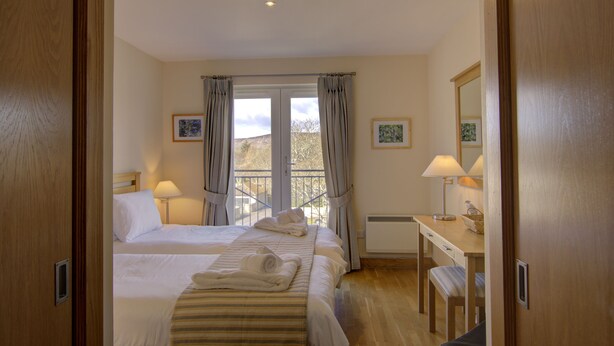 Ein Hotelzimmer mit zwei Betten, einem Schreibtisch und einem Stuhl. Vor den Fenstern hängen Vorhänge, und an der Wand befindet sich ein Bild.