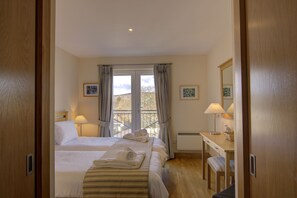 A hotel room with two beds, a desk, and a chair. There are curtains on the windows, and a picture frame on the wall. - No 17 The Links Apartment Brora (Brora)
