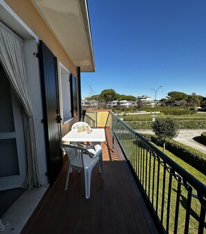 A balcony with a table and chairs, a view of a residential area, and a clear sky. - Family vacation apartment with swimming pools (Bibione)