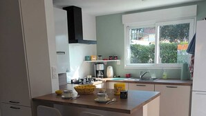A compact kitchen with a central island, two bar stools, a window with a view, and a tiled floor.