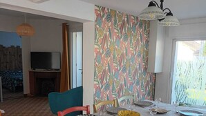 A dining area with a table set for four, chairs, a patterned wall, and a television in the background.