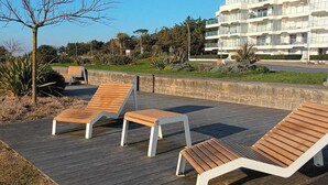 A wooden deck with lounge chairs, a clear sky, and a modern building in the background.
