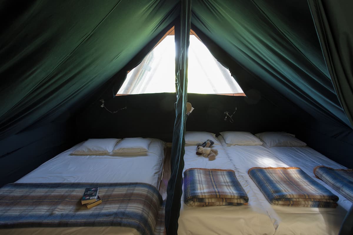 A tent with two beds, each with a pillow and a blanket.
