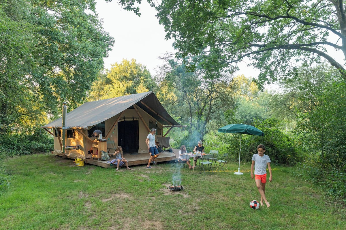 A rustic outdoor setting with a small wooden structure, possibly a cabin or a tent, surrounded by lush greenery.