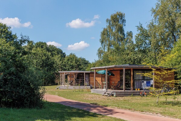 Een houten chalet met een veranda, een overdekte zitplek buiten en een fiets geparkeerd voor de deur.