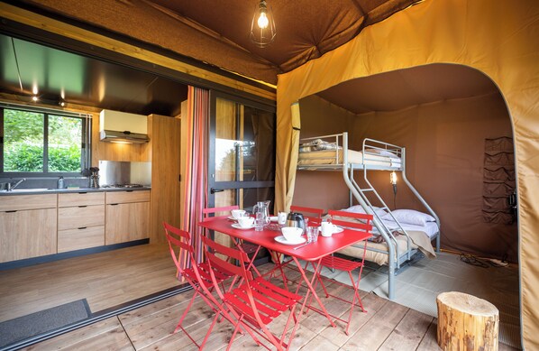 A compact, well-lit tent with a kitchenette, a dining area with red chairs, and a bunk bed. - Huttopia de Roos (Beerze)