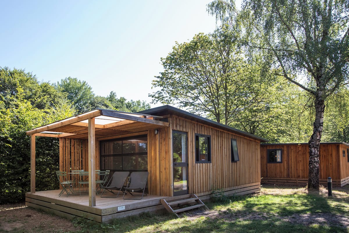 A wooden cabin with a covered patio, a dining area, and a large window.