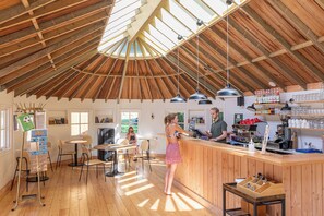 Een gezellig café met houten inrichting, een bar en een zithoek met tafels en stoelen.