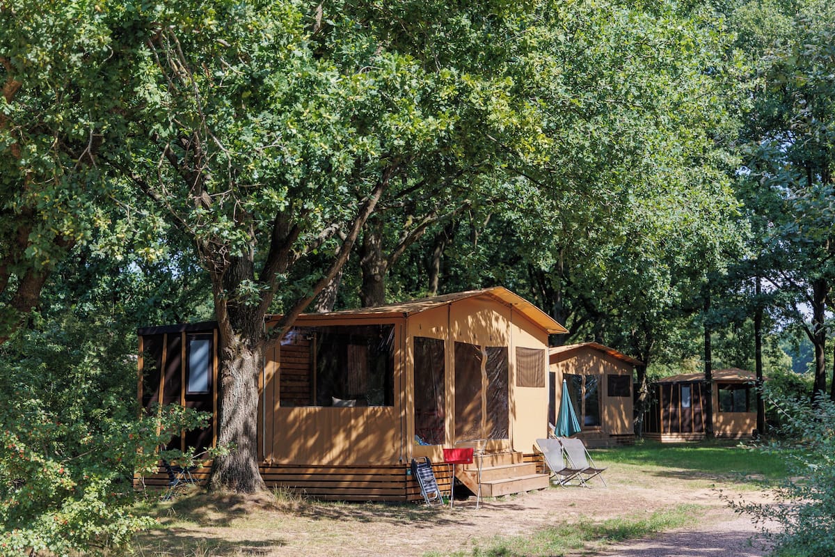 A mobile home with a porch and a small deck, surrounded by trees.
