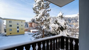 A balcony with snow-covered railings, a yellow building, and a snow-covered tree in the background. - Modern Apartment, Near to Skiing Scenic Lake Views (Sankt Moritz)