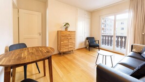 A modern living room with a wooden dining table, a black leather sofa, a small round table, and a wooden cabinet. - Modern Apartment, Near to Skiing Scenic Lake Views (Sankt Moritz)