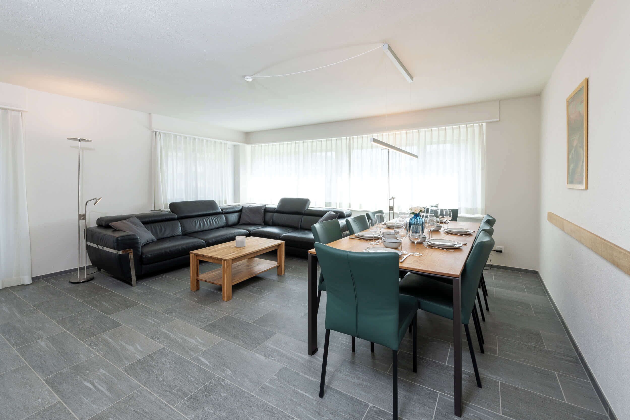A modern living room with a black leather sofa, a wooden coffee table, and a dining area with a table set for four.