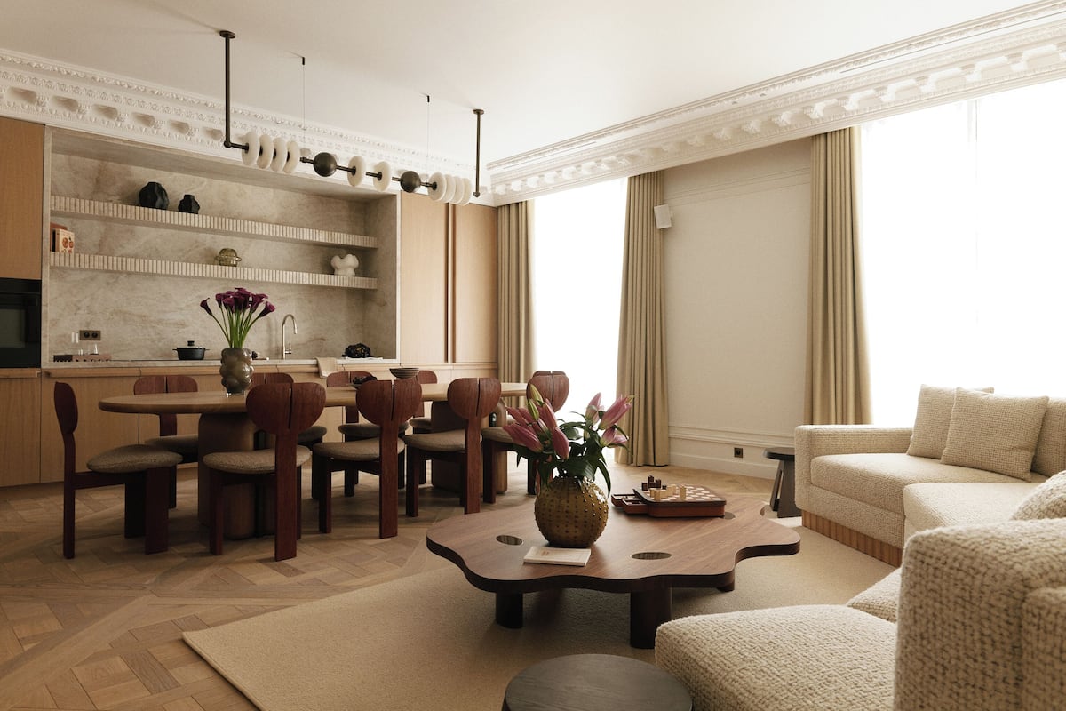 A modern living room with a dining area, a kitchen in the background, and large windows with curtains.