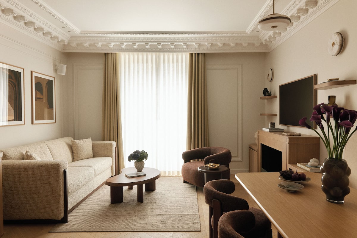 A living room with a sofa, armchairs, a coffee table, a TV, and a vase with flowers.