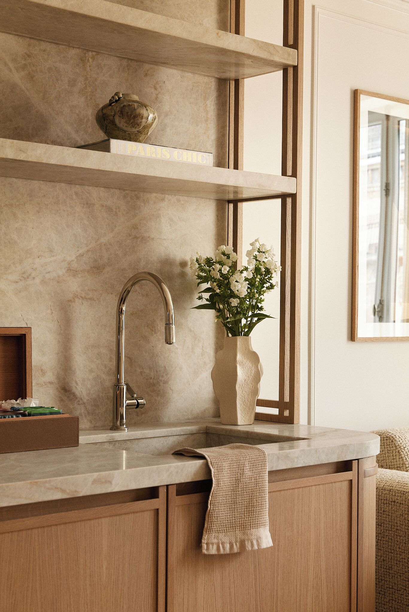 Una cocina con un grifo moderno, un florero con flores y estantes de madera.