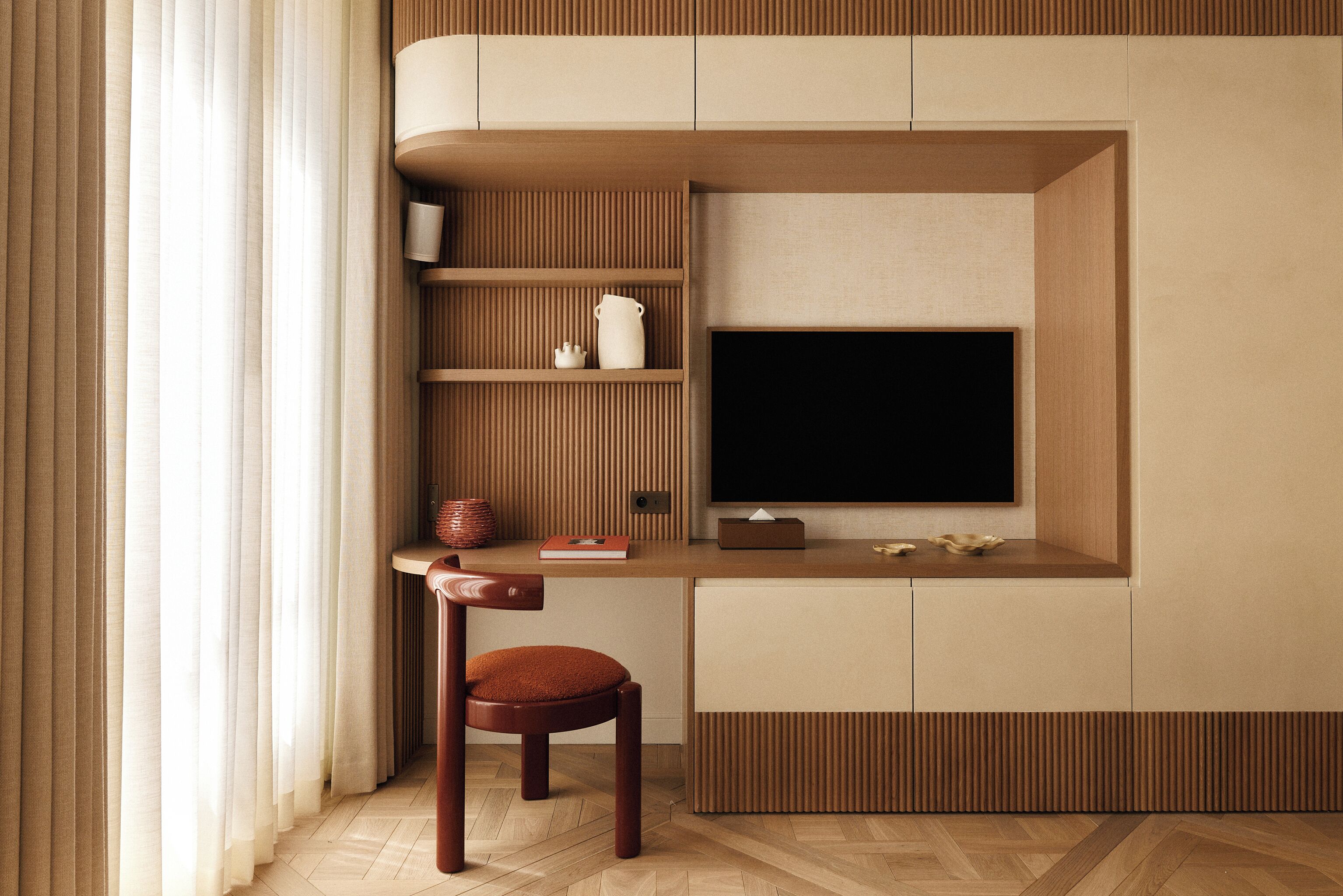 A modern, compact living space with a built-in TV, wooden paneling, a small table, and a cushioned chair.