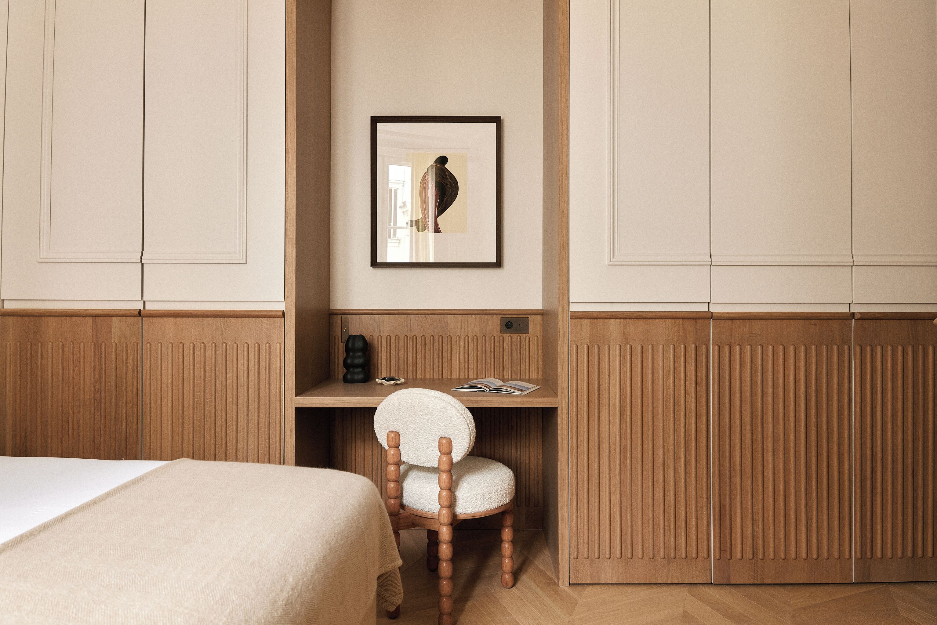 A hotel room with a bed, a wooden desk, a chair, and a framed picture on the wall.
