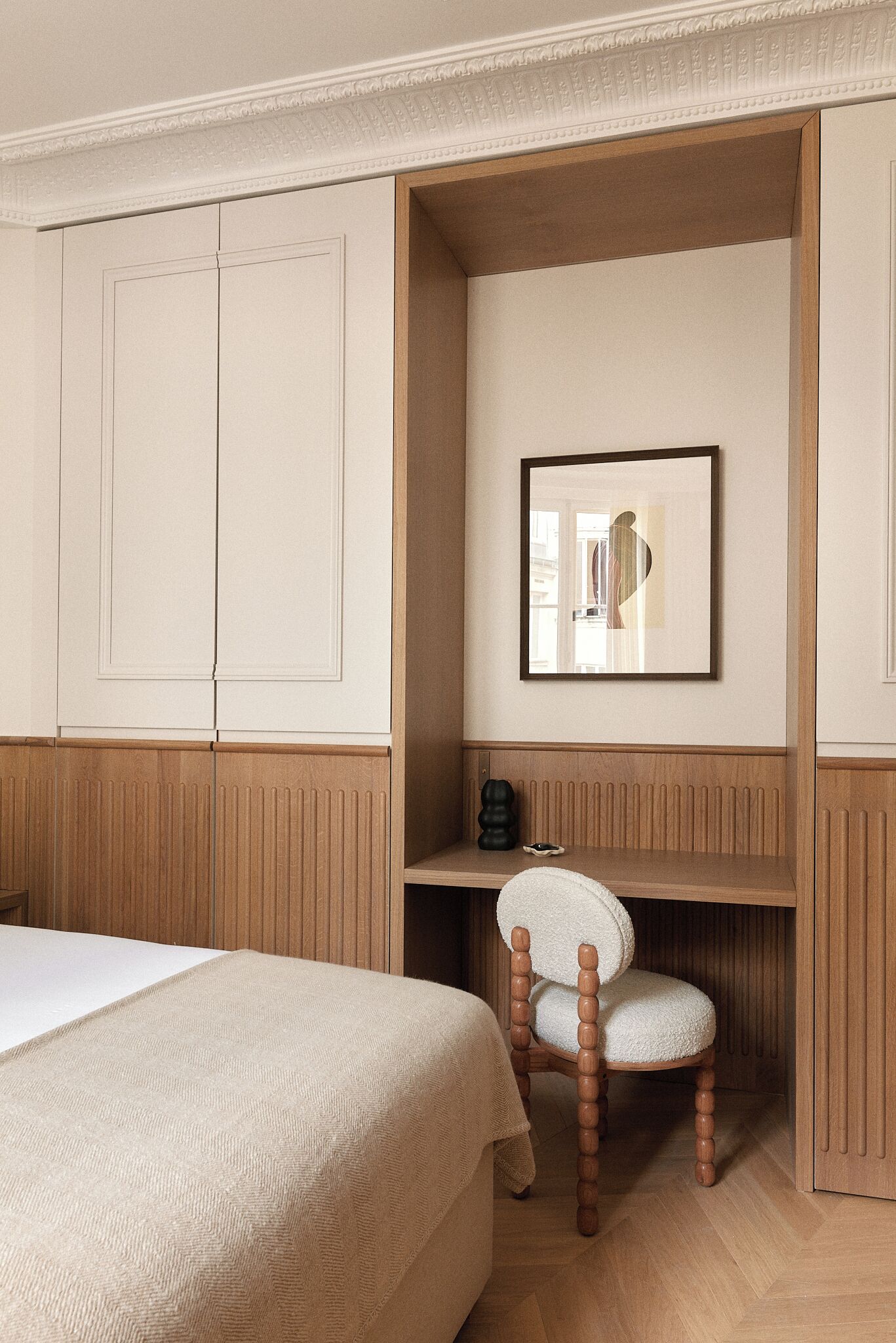 A bedroom with a bed, a wooden chair, a desk, and a framed picture on the wall.