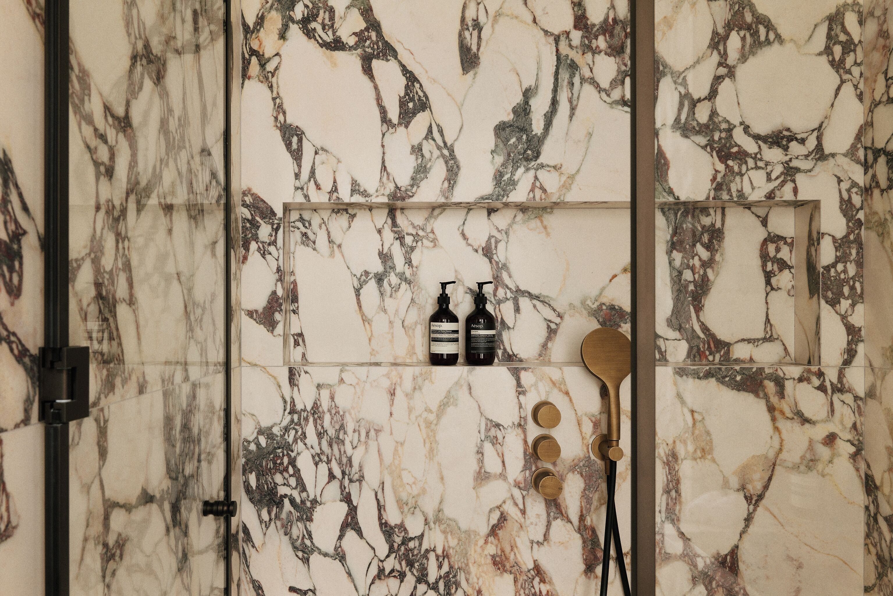 Ein Badezimmer mit Marmorwand, zwei Shampoo-Flaschen und einer Holzbadematte.