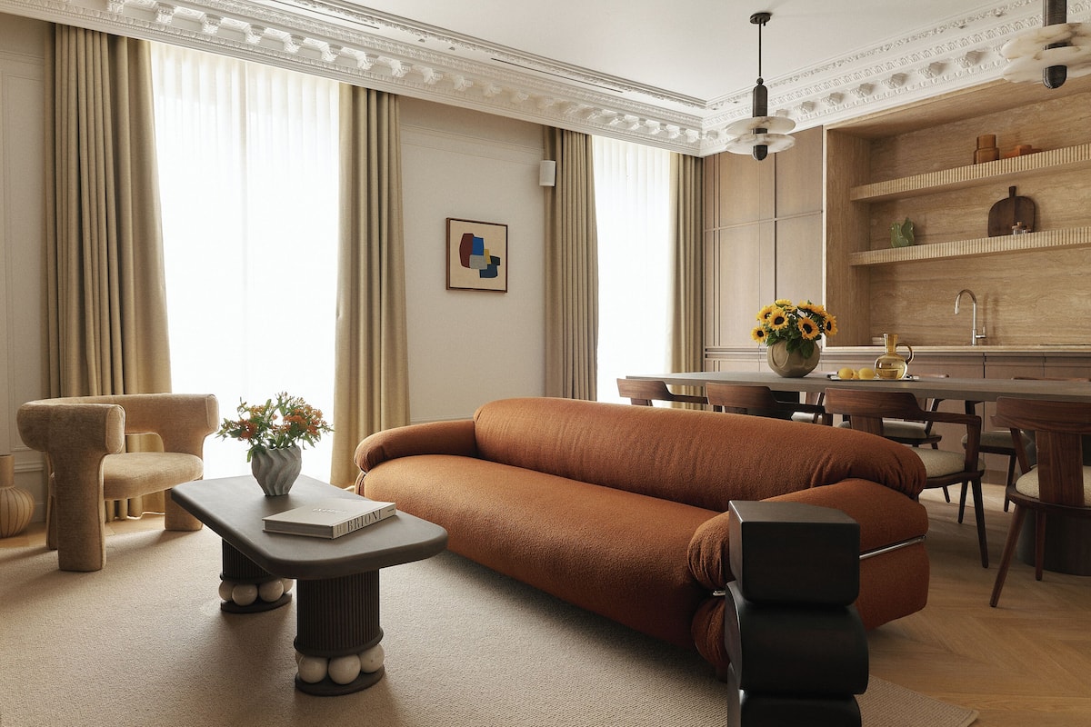 A modern living room with a brown sofa, a coffee table, and a dining area with a wooden table and chairs.