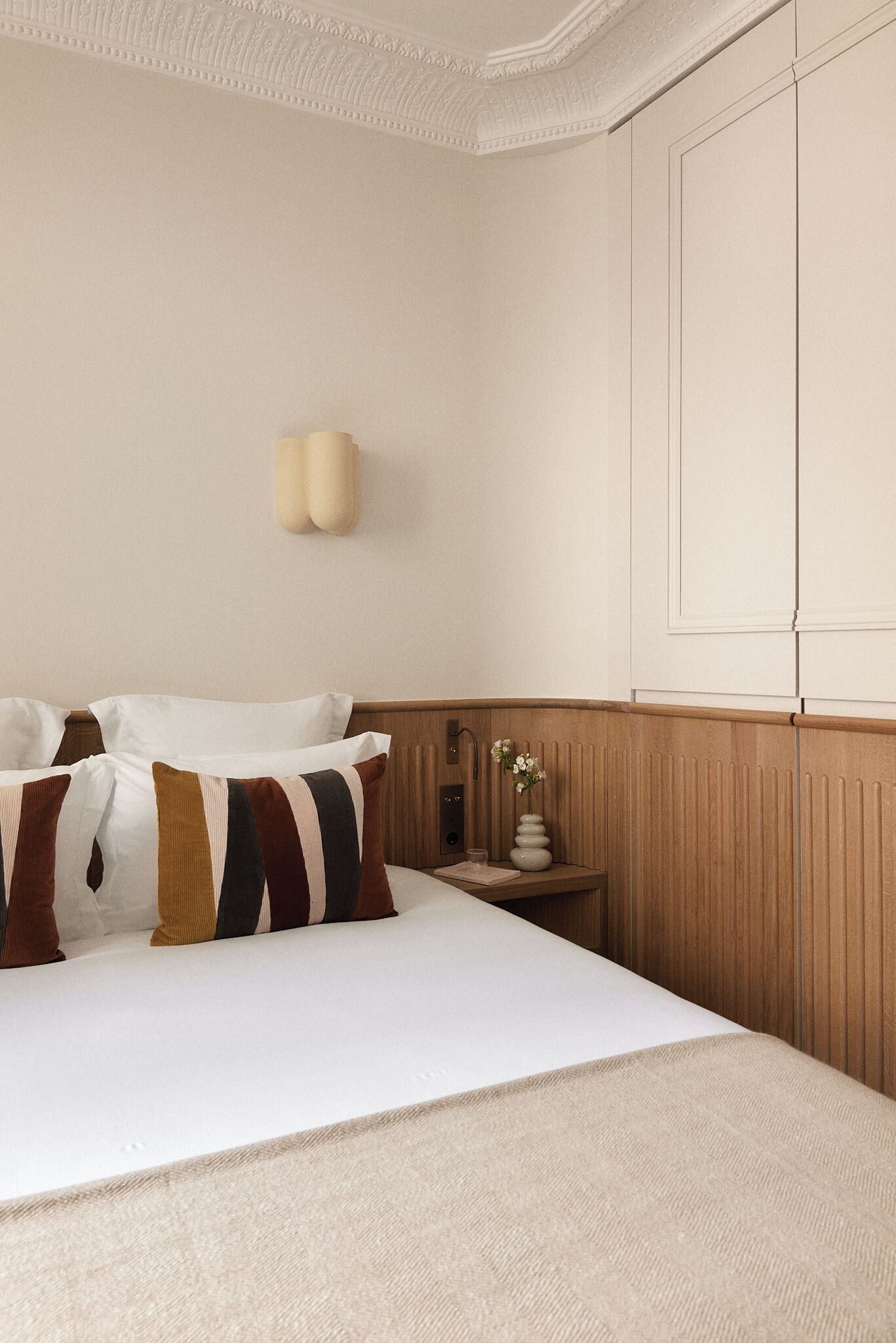 Un dormitorio ordenado con cama, almohadas, una mesita de noche y una lámpara de pared.