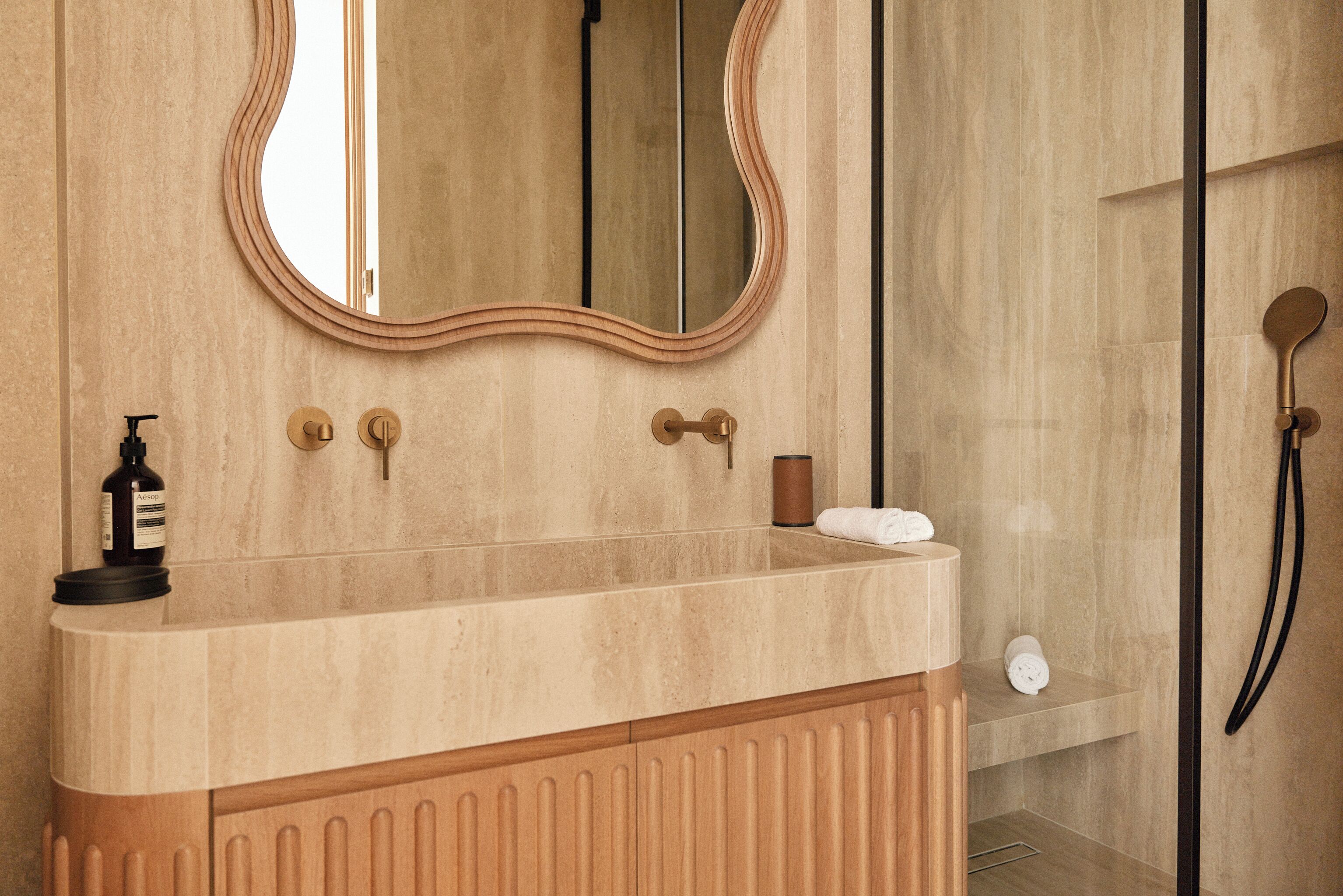 A bathroom with a wooden vanity, a large mirror, a towel rack, and a shower area.