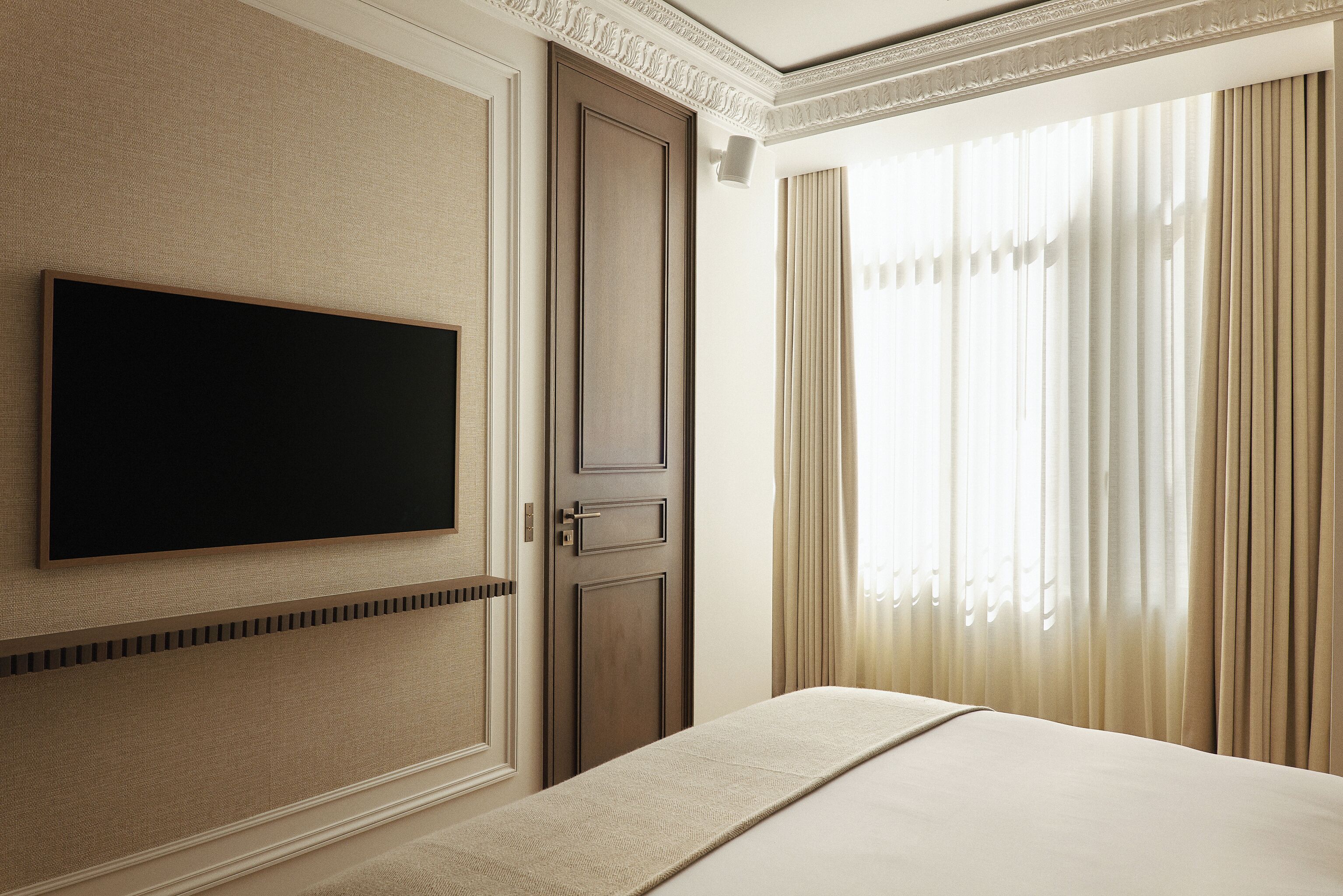 Een hotelkamer met een grote flatscreen televisie aan de muur, een deur met een handgreep en een raam met gordijnen.