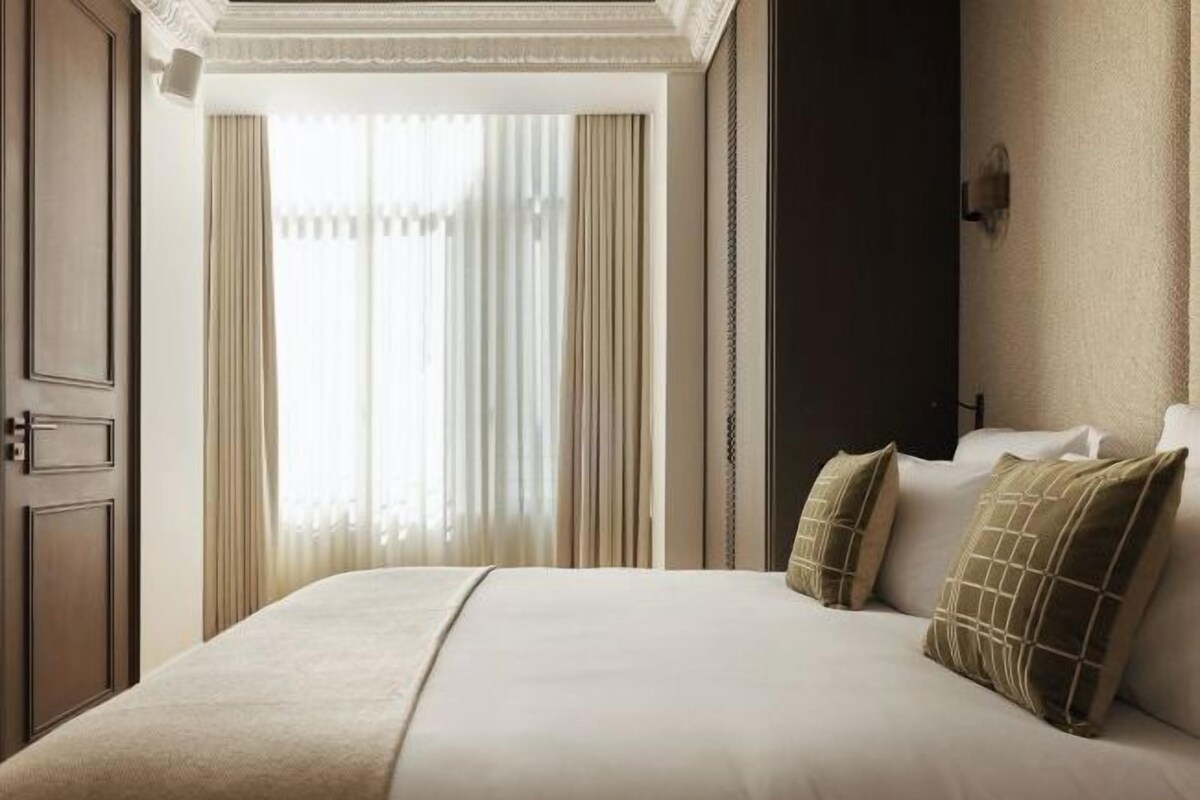 Ett hotellrum med en stor säng, beige gardiner och en mörk dörr.