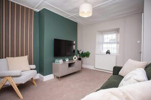 Una sala de estar con sofá, televisor, mueble, planta y ventana.