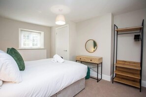 A bedroom with a bed, a bedside table, a mirror, a window, and a wardrobe.