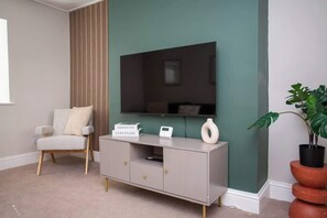 Una habitación con un mueble gris para entretenimiento, un televisor, una silla y una planta en maceta.