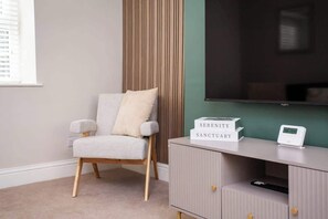 A room with a grey armchair, a cabinet with a thermostat, and a wall-mounted TV. - Castle Hill | Wi-Fi | Parking (Northumberland)