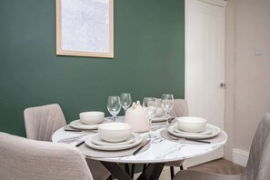 A dining table set with white plates, bowls, and glasses, surrounded by chairs, with a framed picture on the wall. - Castle Hill | Wi-Fi | Parking (Northumberland)