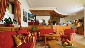 A cozy living room with a sofa, chairs, a coffee table, and a kitchen area with wooden cabinets and a television.