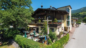 A traditional chalet-style building with multiple balconies, outdoor seating, and a mountain backdrop.