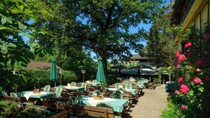 An outdoor dining area with tables and chairs, surrounded by greenery and flowers.
