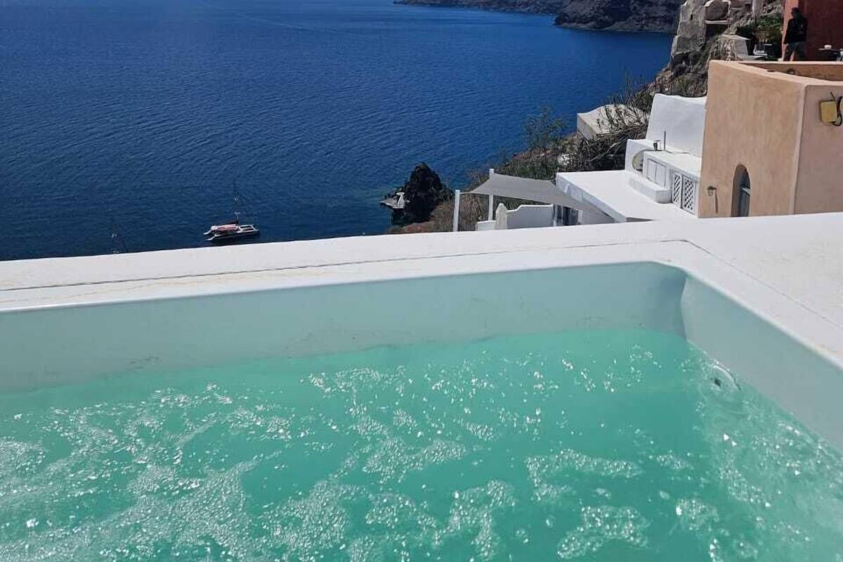 Vista di una zona costiera con mare cristallino, un edificio bianco dotato di piscina e terreno roccioso sullo sfondo.