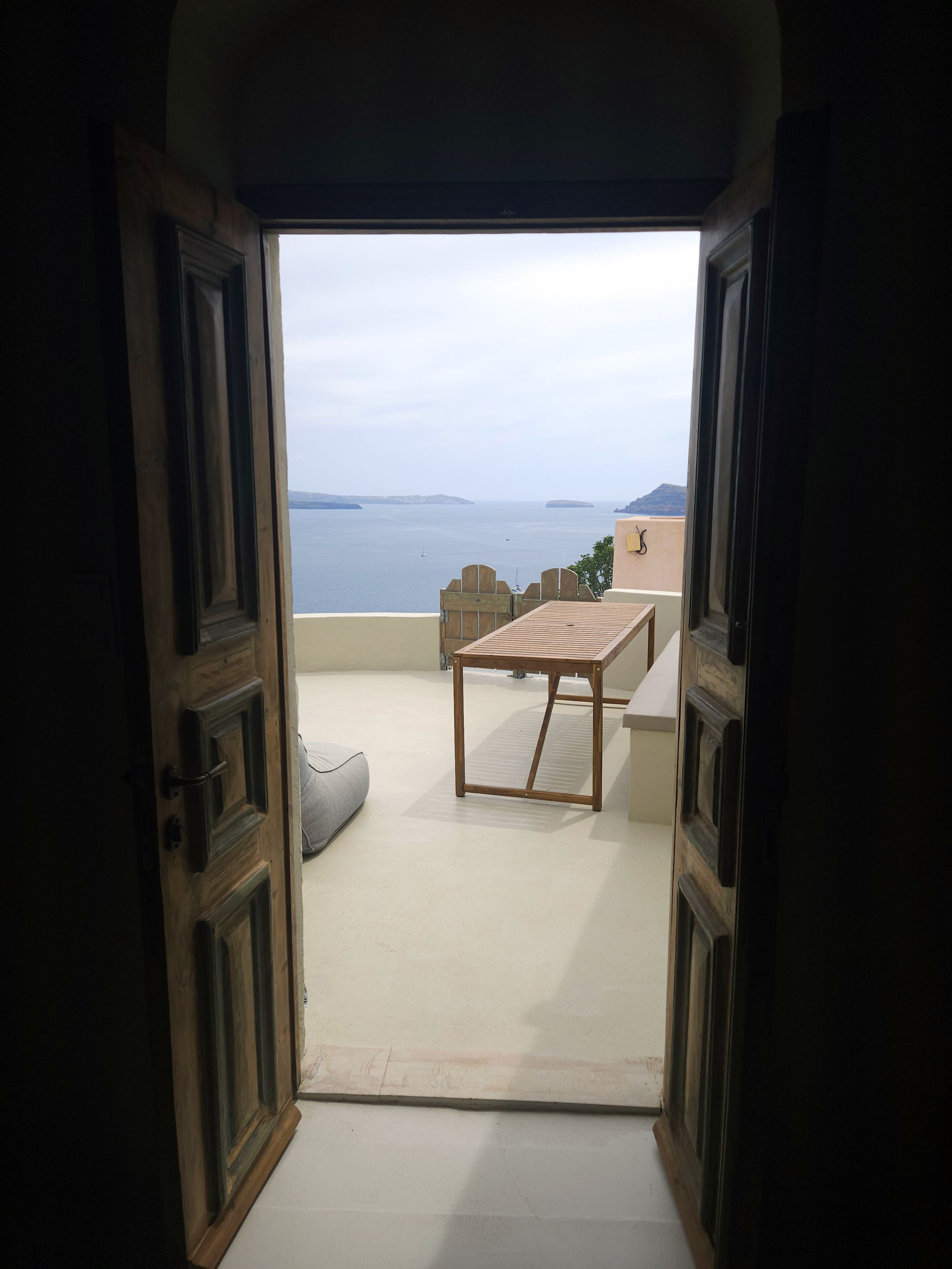 Une porte ouverte donne sur un balcon où se trouvent une table et des chaises, d’où l’on peut admirer un plan d’eau et le paysage lointain.