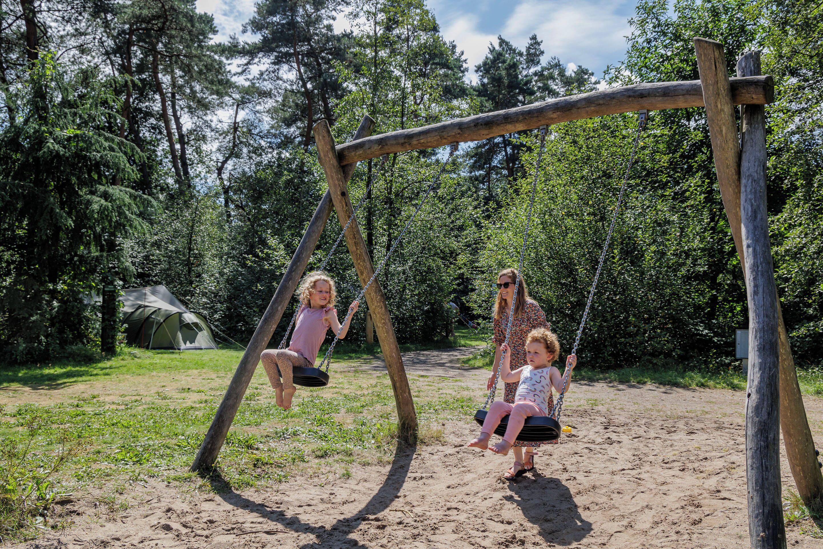 A wooden swing set in a natural setting with a tent in the background.