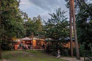 Restaurante ao ar livre com mesas e cadeiras, cercado por árvores e um cercado de madeira.