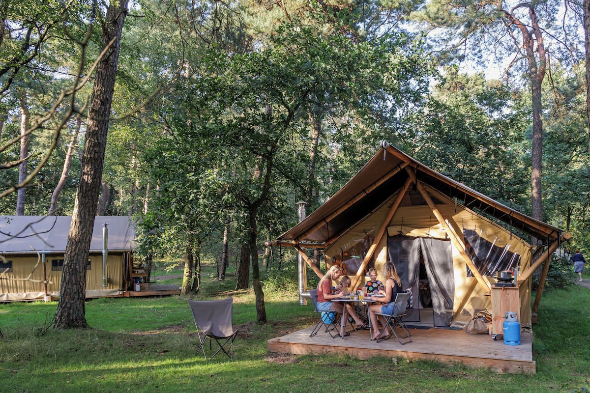 A rustic wooden tent with a dining area and a small deck, surrounded by trees.