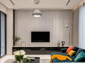 A modern living room with a large flat-screen TV mounted on a wooden wall, a sofa with colorful cushions, a coffee table with a vase of flowers, and a floor lamp. - Luxury City View Apartment in London (London)
