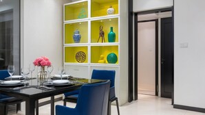 A modern dining area with a black table, blue chairs, and a yellow and white display unit with decorative items.