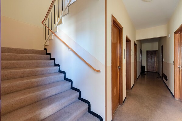A carpeted staircase with a wooden handrail leading to a landing. A hallway with wooden doors and a light-colored floor extends from the landing. - Cosy flat with terrace (Rapallo)