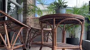 A wicker outdoor seating area with a woven rug, potted plants, and a brick wall.