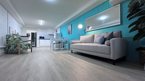 A modern living room with a sofa, a dining table, and a kitchen in the background.