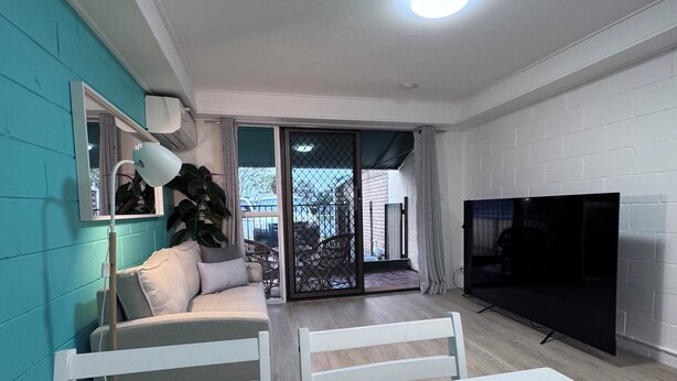 A modern living room with a sofa, TV, and dining area with a table set for two.